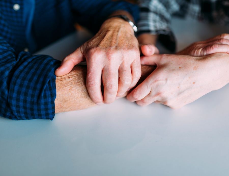 Las manos de una hija sostienen las de su madre sobre la mesa